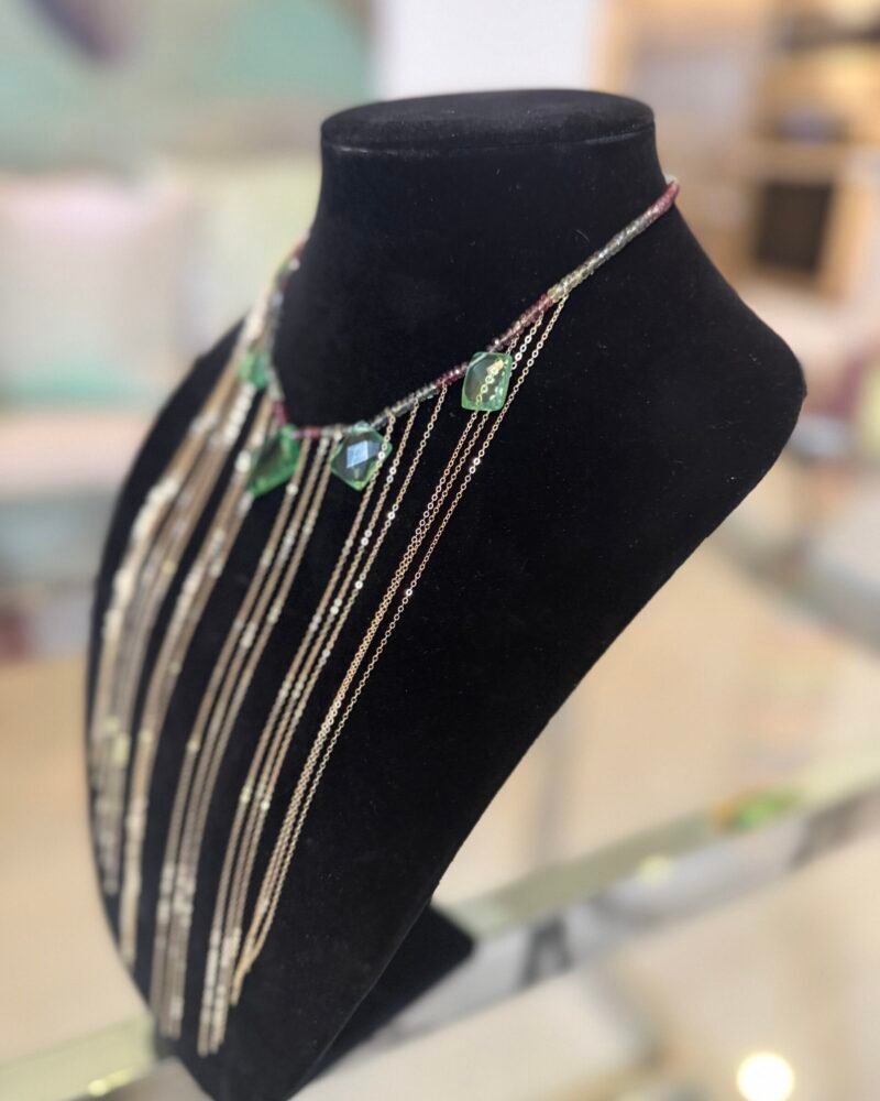 “FN037 necklace by Fausette featuring a sapphire rondelle strand, oversized pillow-cut green amethyst stones, and nineteen 8-inch 14k gold rolo chain fringe drops displayed on black bust.”